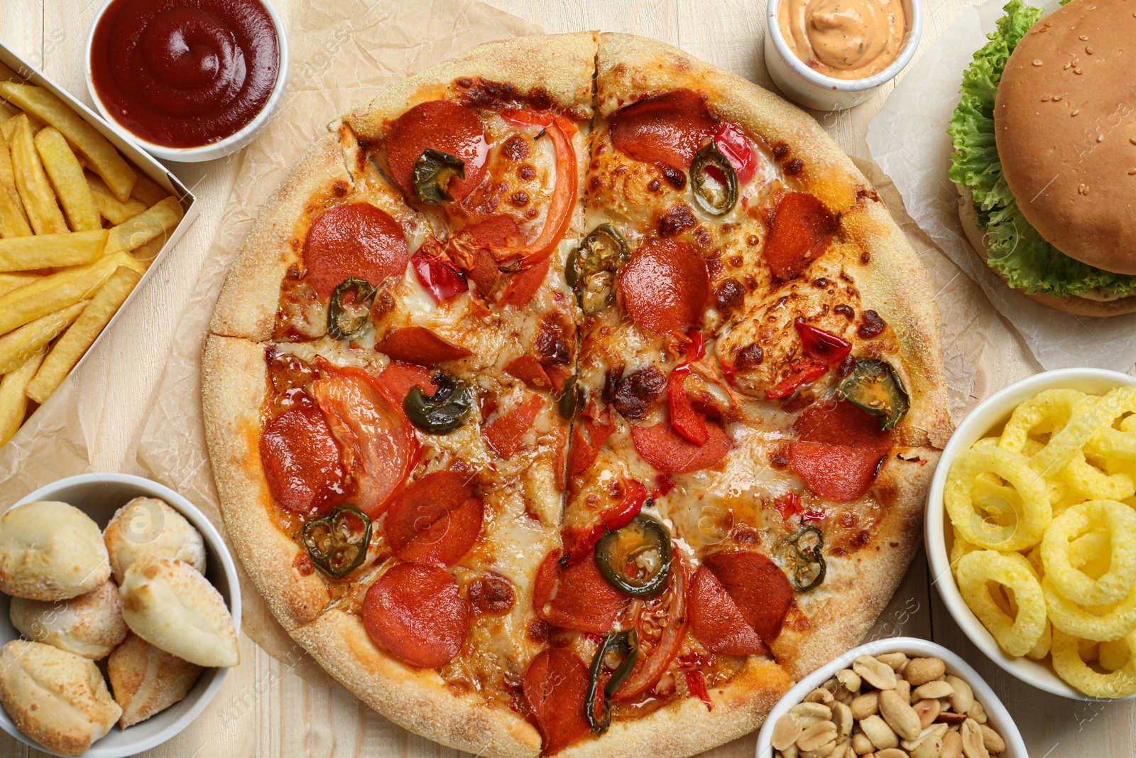 Photo of Pizza, onion rings and other fast food on wooden table, flat lay