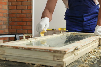 Photo of Man repairing old damaged window at table indoors, closeup