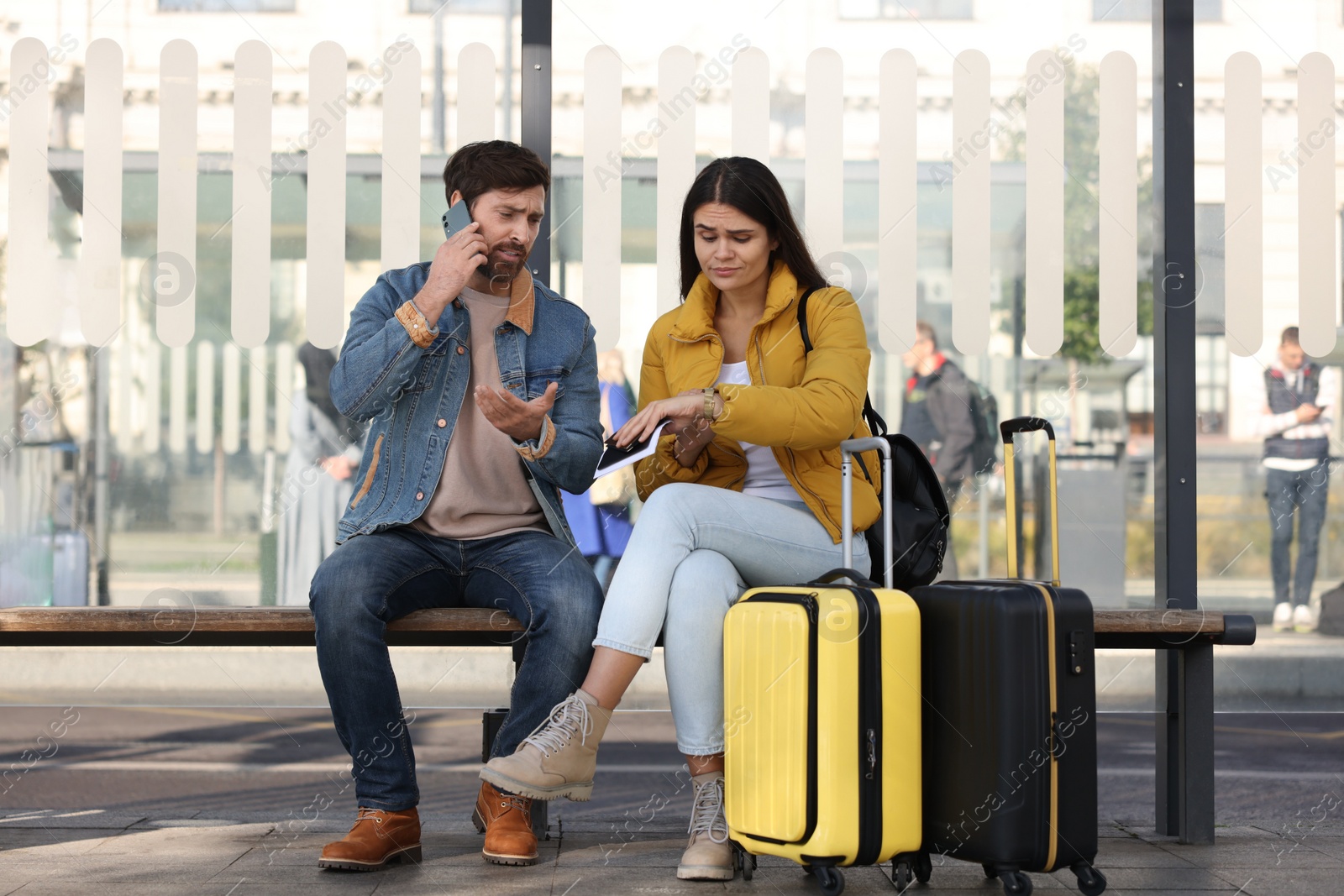 Photo of Being late. Worried couple with suitcases sitting at bus station outdoors