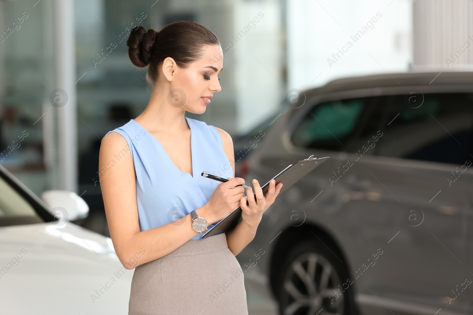 Photo of Young saleswoman with clipboard in car dealership