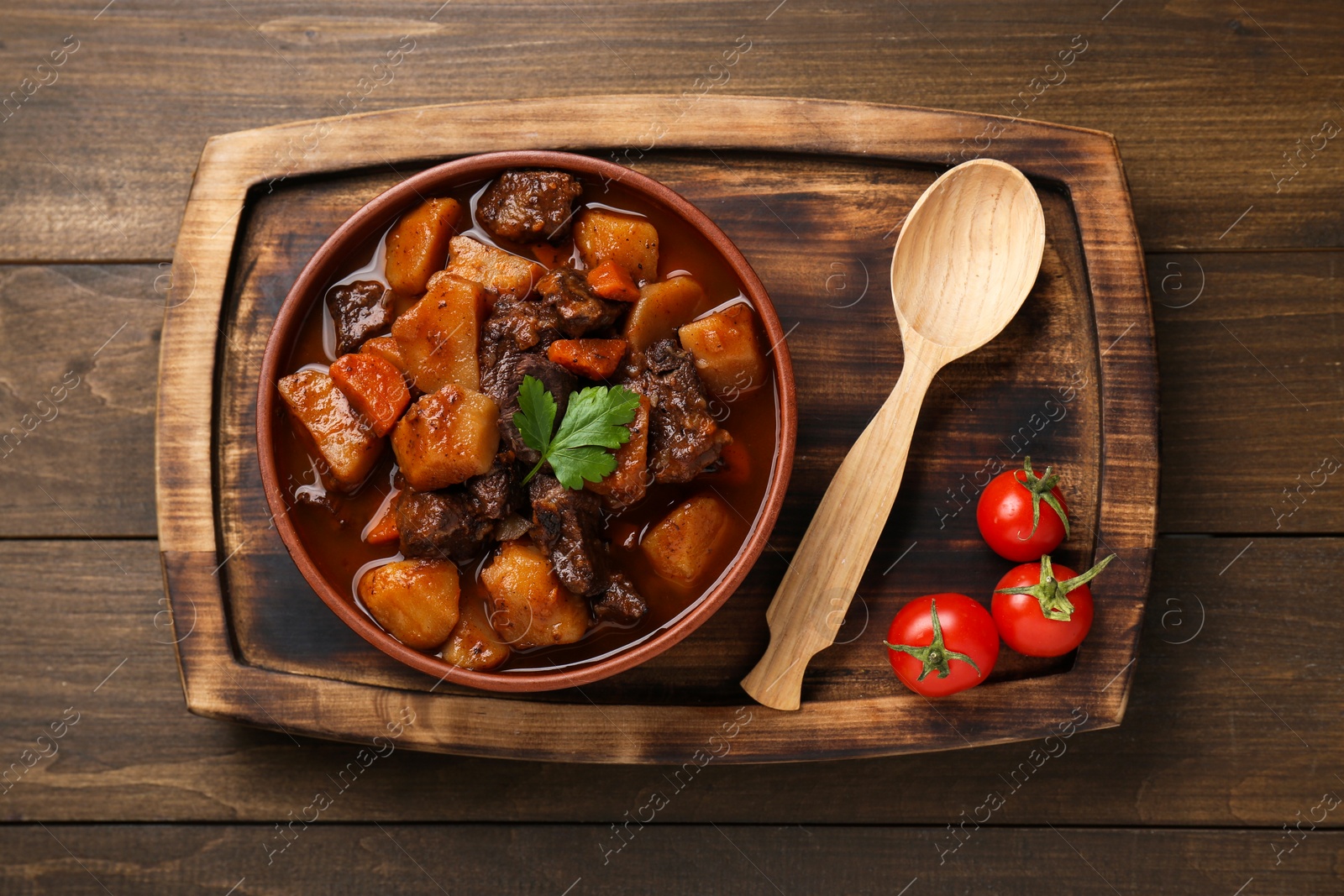 Photo of Delicious beef stew with carrots, parsley and potatoes on wooden table, top view