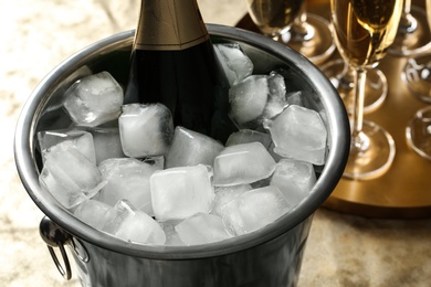 Bottle of champagne in bucket with ice cubes on table, closeup