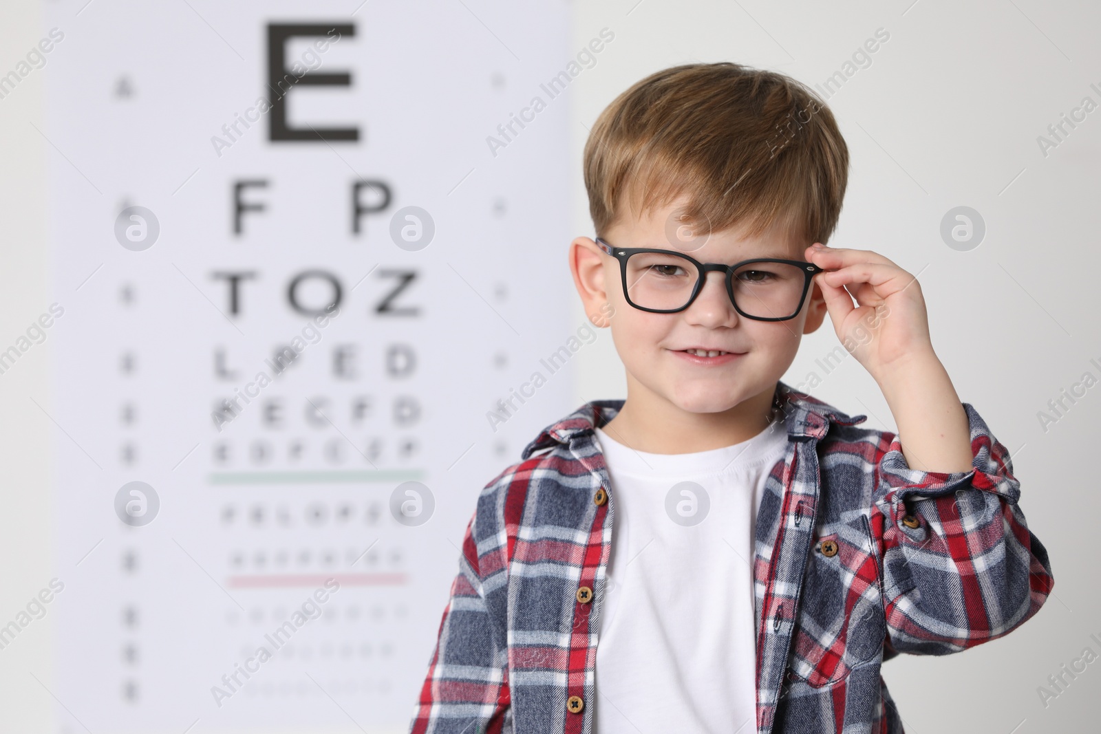 Photo of Little boy with glasses against vision test chart