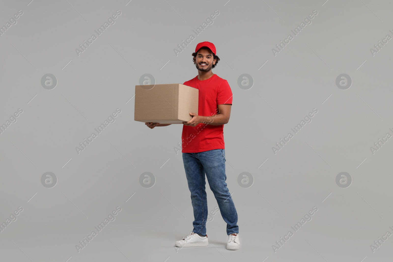 Photo of Happy young courier with parcel on grey background