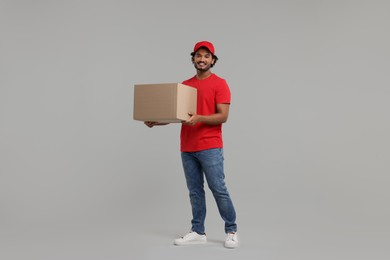 Happy young courier with parcel on grey background