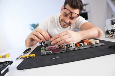 Photo of Male technician repairing motherboard at table indoors