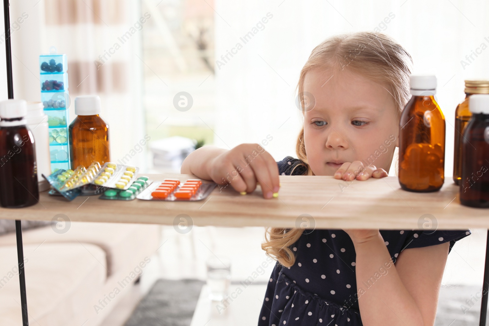 Photo of Little child taking pills from shelf at home. Danger of medicament intoxication