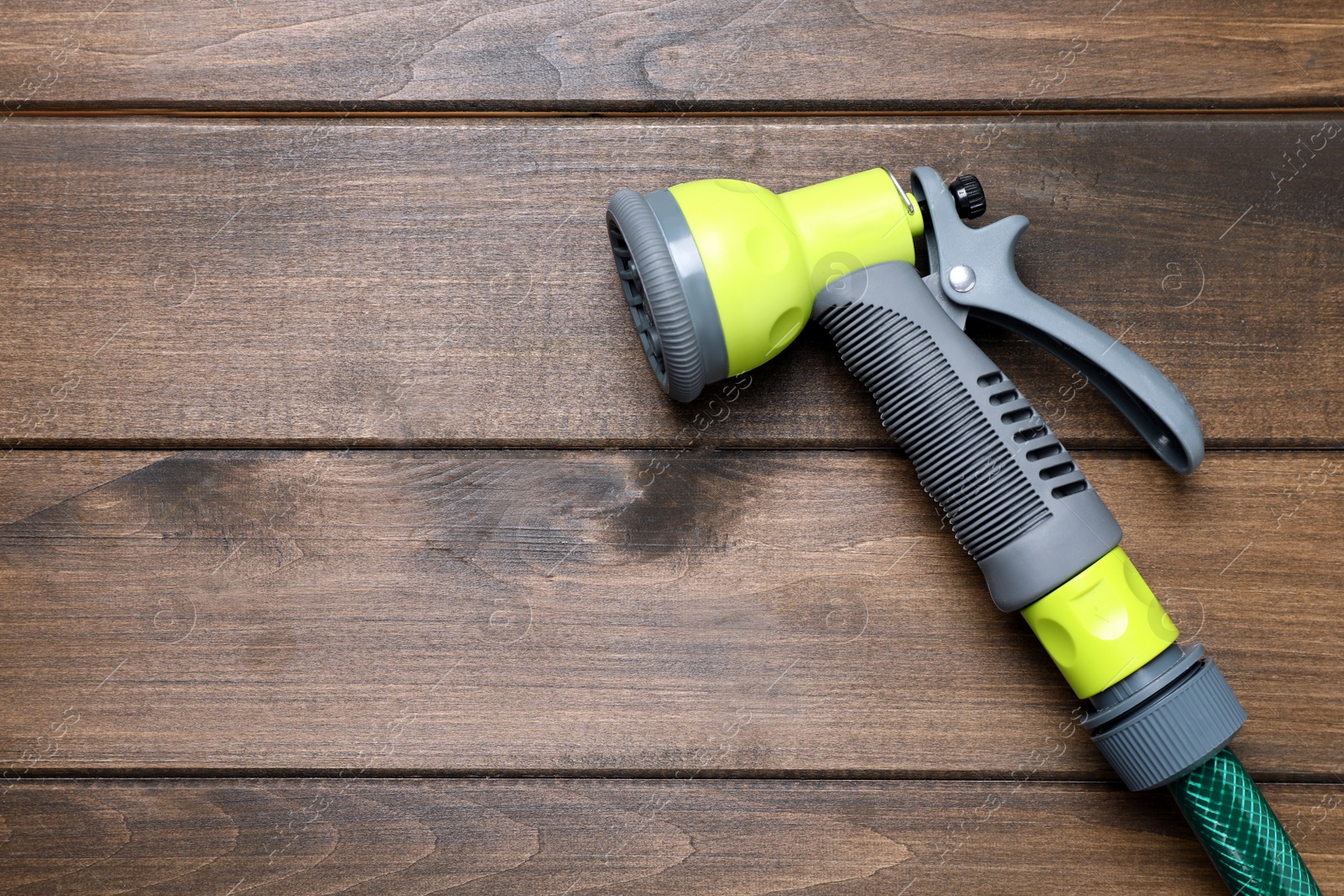 Photo of Green garden hose with spray gun on wooden table, top view. Space for text