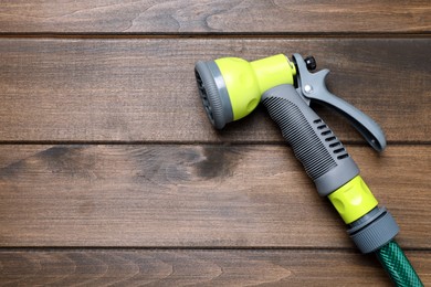 Green garden hose with spray gun on wooden table, top view. Space for text