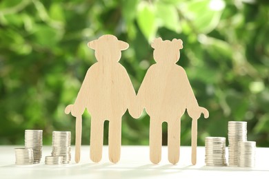 Photo of Pension savings. Figure of senior couple and stacked coins on white wooden table outdoors