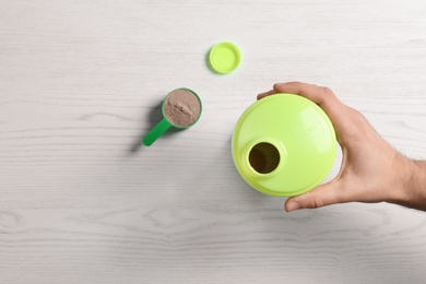 Woman with bottle of protein shake at wooden table, top view. Space for text