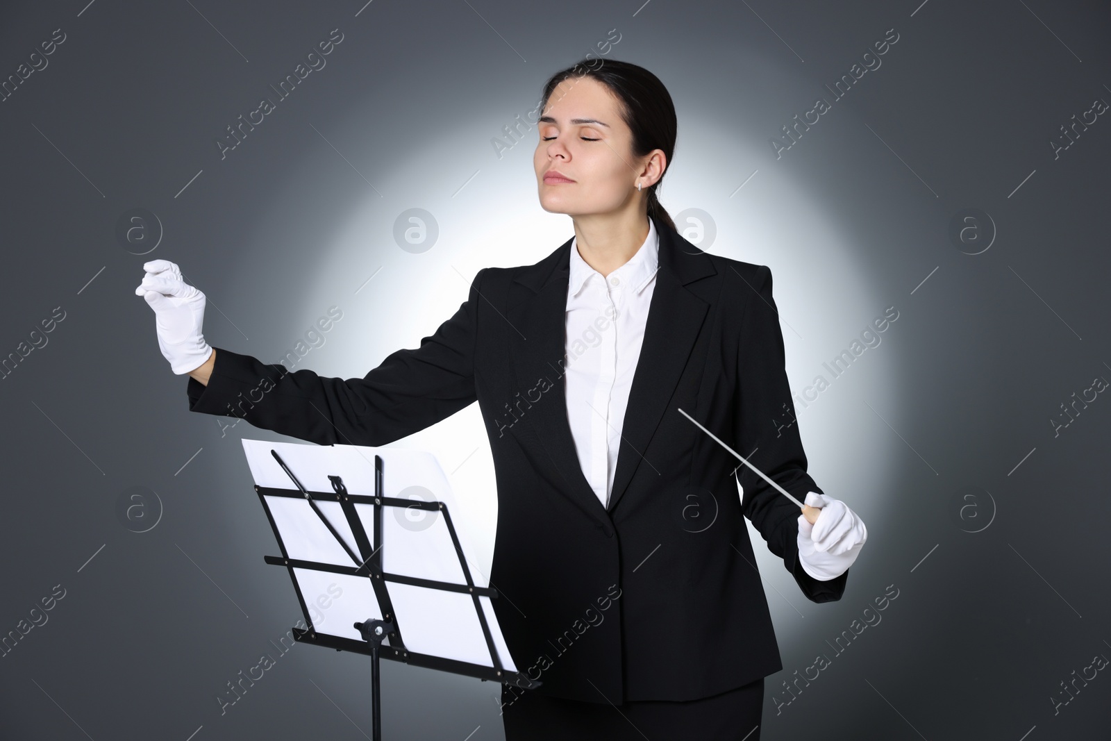 Photo of Professional conductor with baton and note stand on grey background