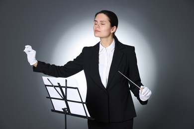 Professional conductor with baton and note stand on grey background