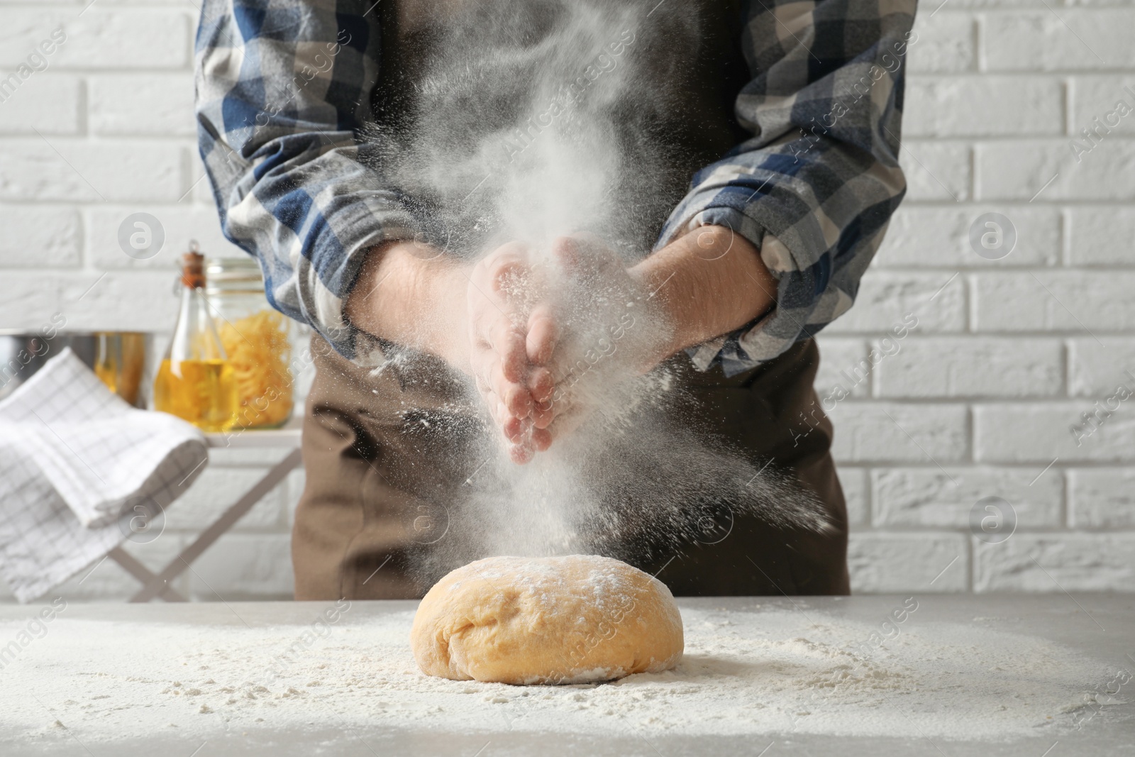 Photo of Young man sprinkling flour on dough for pasta at table