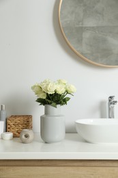 Photo of Vase with beautiful white roses and toiletries near sink in bathroom