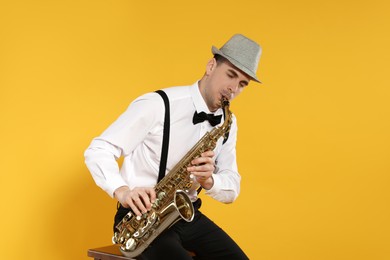 Young man in elegant outfit playing saxophone on yellow background