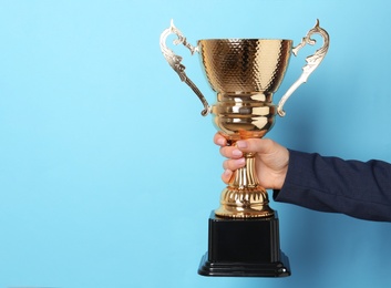 Photo of Woman holding golden trophy cup on color background, closeup. Space for text