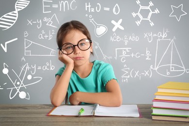Image of Bored little girl doing homework at wooden table and different formulas against light grey background