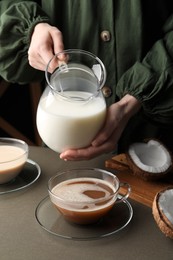 Woman holding tasty coconut milk near cups with coffee at table, closeup