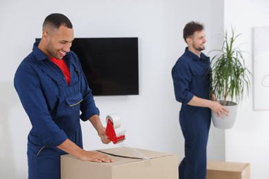 Photo of Male mover packing box with adhesive tape in house, space for text