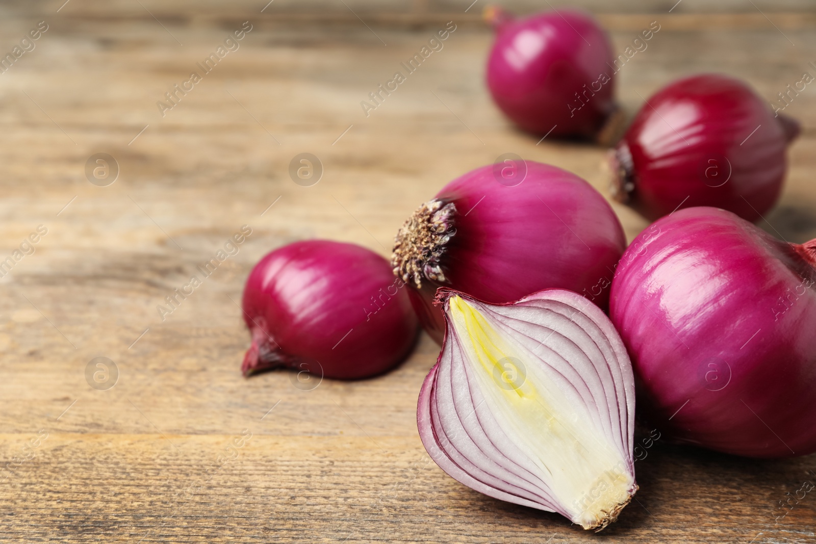 Photo of Ripe red onion bulbs on wooden table, closeup