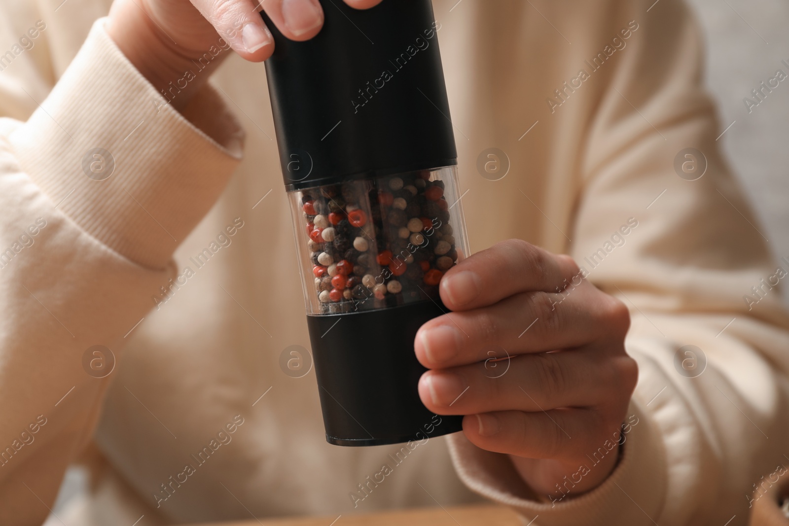 Photo of Woman grinding pepper with shaker at table, closeup