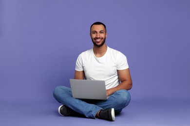 Smiling young man working with laptop on lilac background