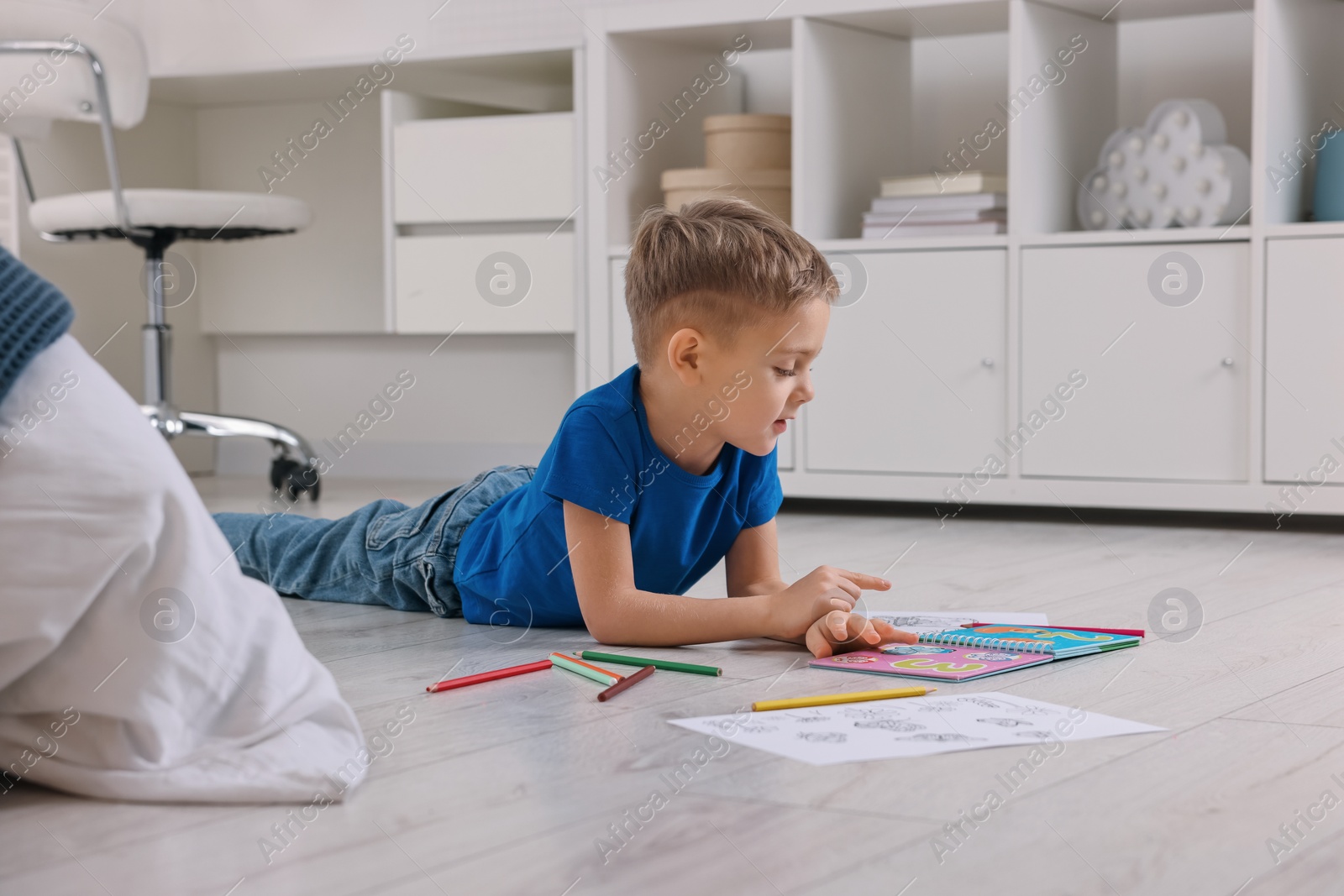 Photo of Cute little boy reading book on warm floor at home. Heating system