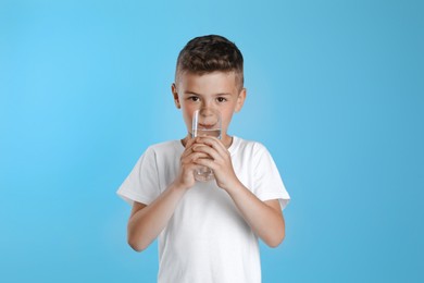 Photo of Cute little boy drinking water from glass on light blue background