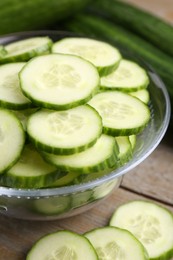 Cut cucumber in glass bowl and fresh vegetables on wooden table, closeup