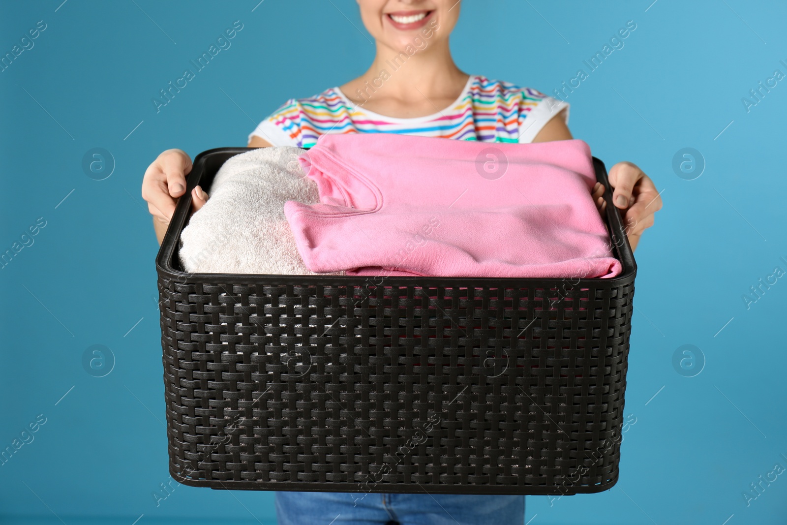Photo of Young woman holding basket with clothes on color background, closeup