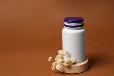 Photo of Medicine bottle near gypsophila flowers on brown background, space for text