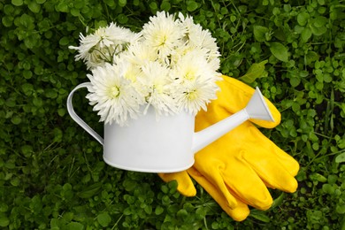Gardening gloves and watering can with flowers on green grass, flat lay