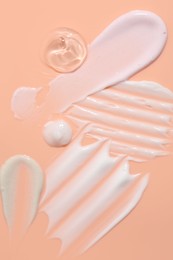 Photo of Samples of face cream on coral background, top view