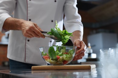 Photo of Professional chef making salad in restaurant kitchen, closeup