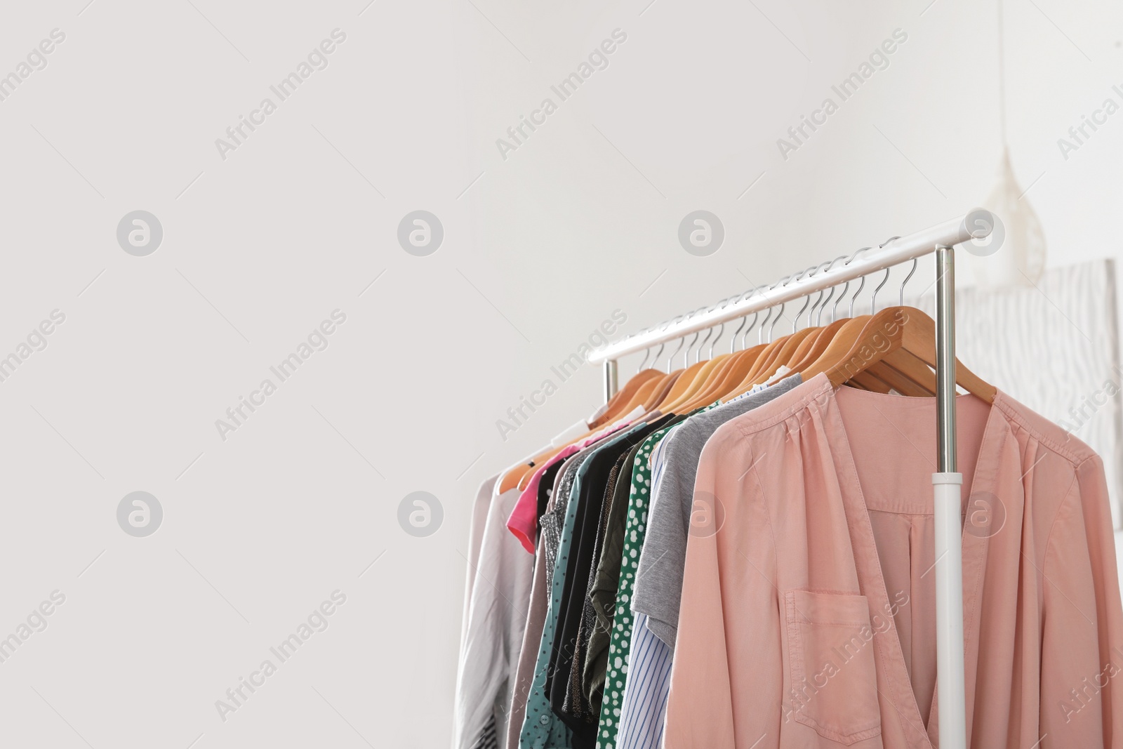 Photo of Wardrobe rack with stylish clothes near white wall indoors. Space for text