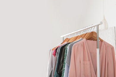 Wardrobe rack with stylish clothes near white wall indoors. Space for text