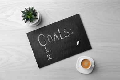 Photo of Slate board with word Goals, numbering, houseplant and cup of coffee on white wooden table, flat lay. Planning concept