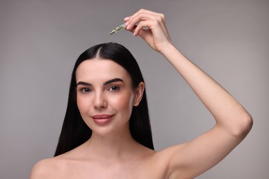 Photo of Beautiful young woman using ampoule for hair treatment on grey background