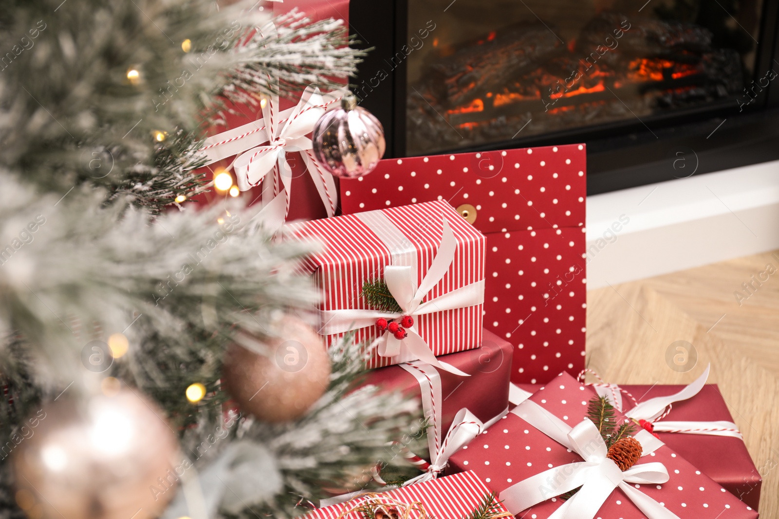 Photo of Many different gifts near Christmas tree and fireplace indoors