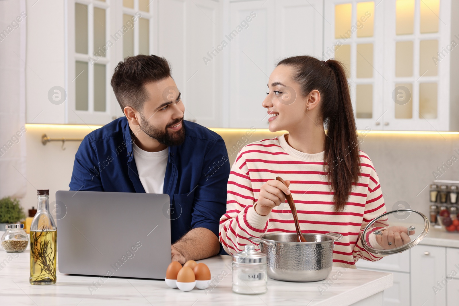 Photo of Happy lovely couple using laptop while cooking in kitchen