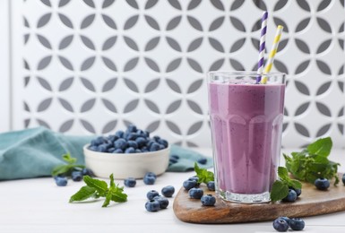 Glass of blueberry smoothie with mint and fresh berries on white wooden table, space for text