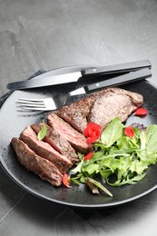 Photo of Delicious grilled beef meat served with greens on grey table