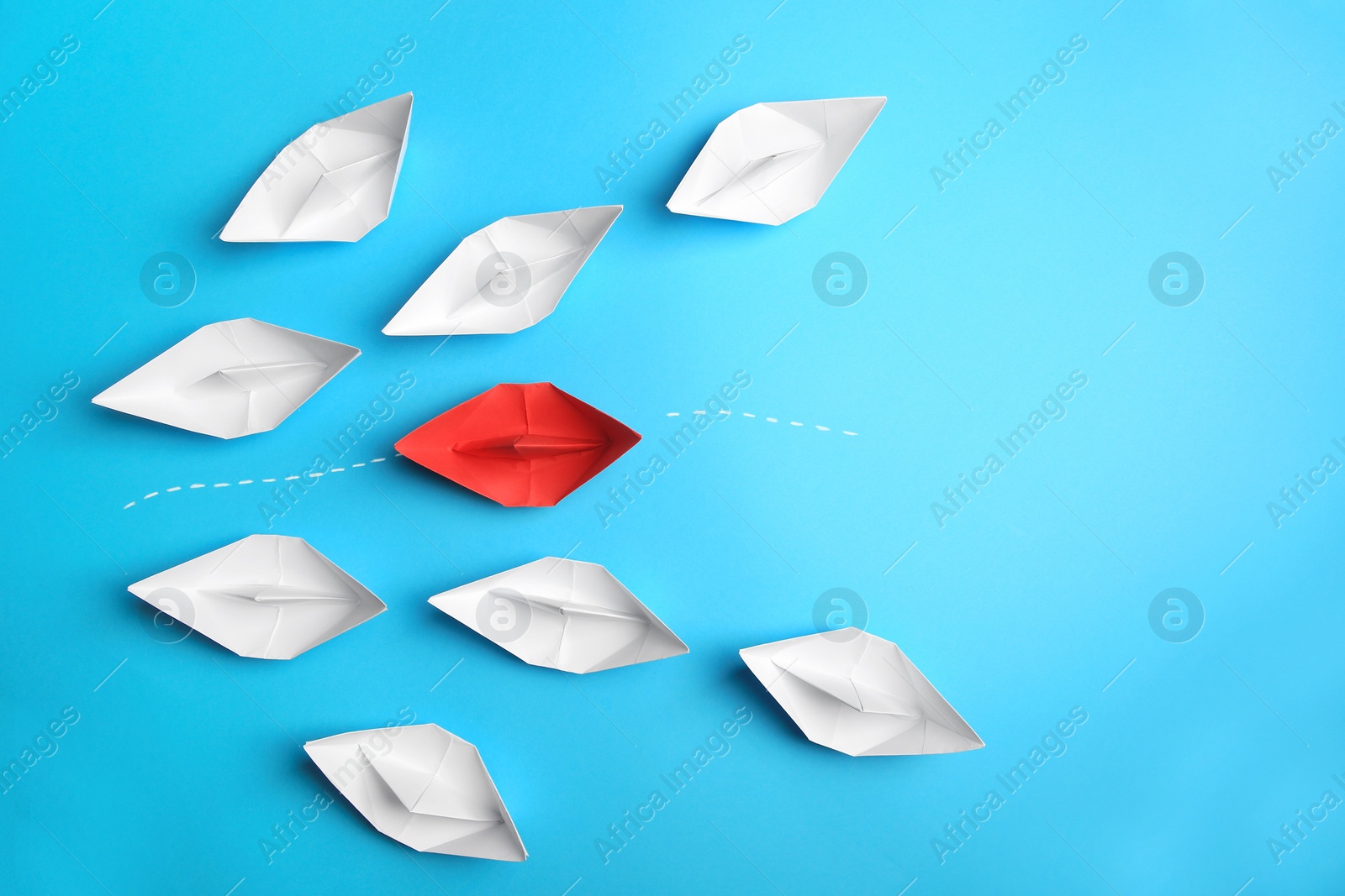 Photo of Red paper boat floating between others on light blue background, flat lay with space for text. Uniqueness concept