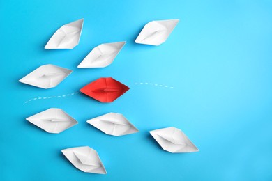 Photo of Red paper boat floating between others on light blue background, flat lay with space for text. Uniqueness concept