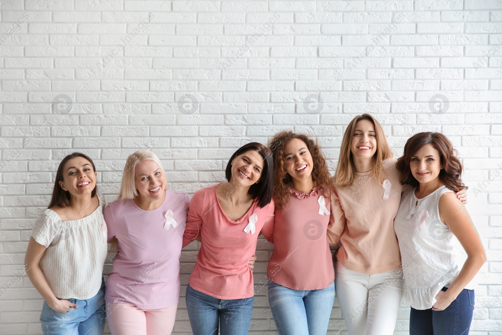 Photo of Group of women with silk ribbons near brick wall. Breast cancer awareness concept