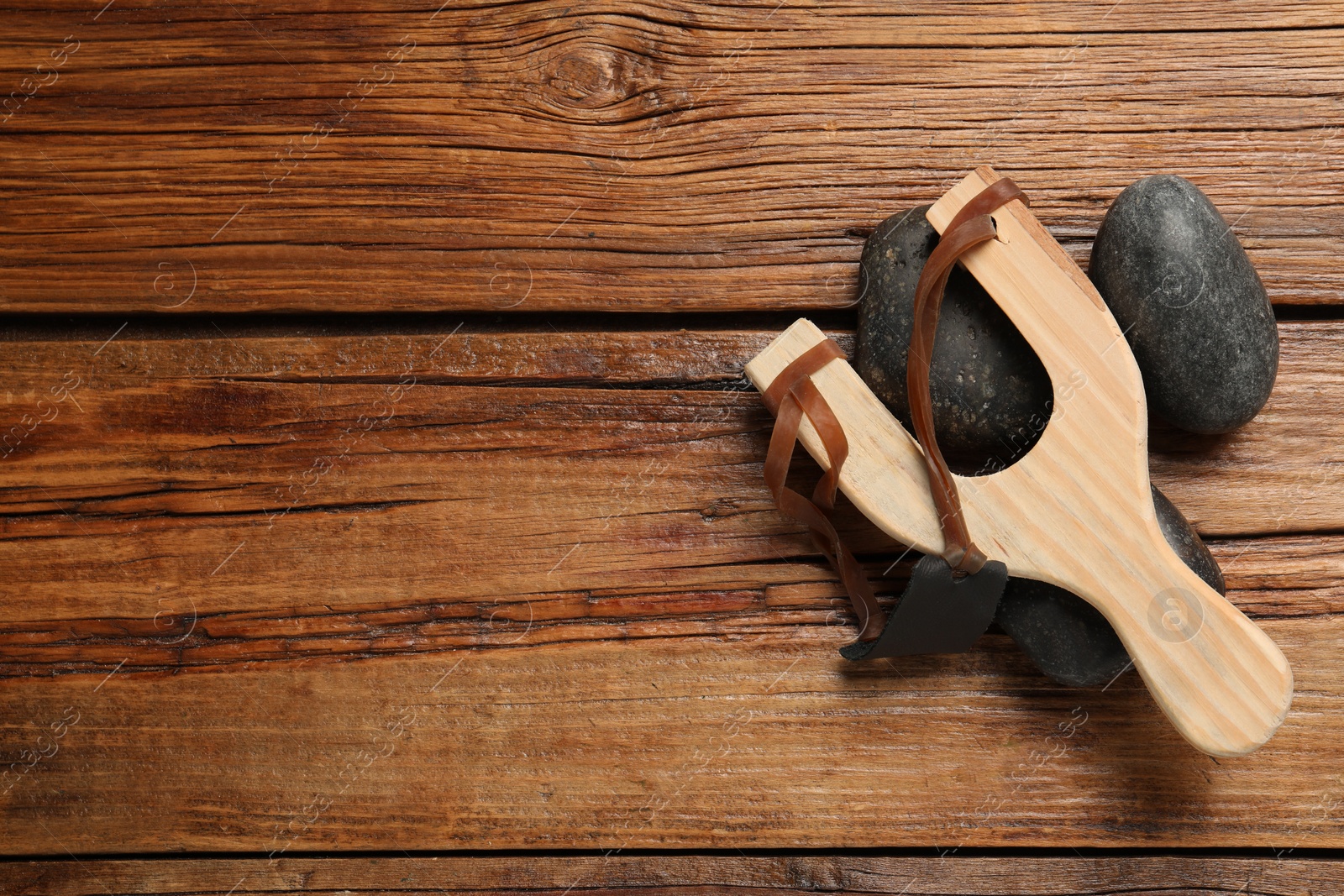 Photo of Slingshot with stones on wooden background, flat lay. Space for text