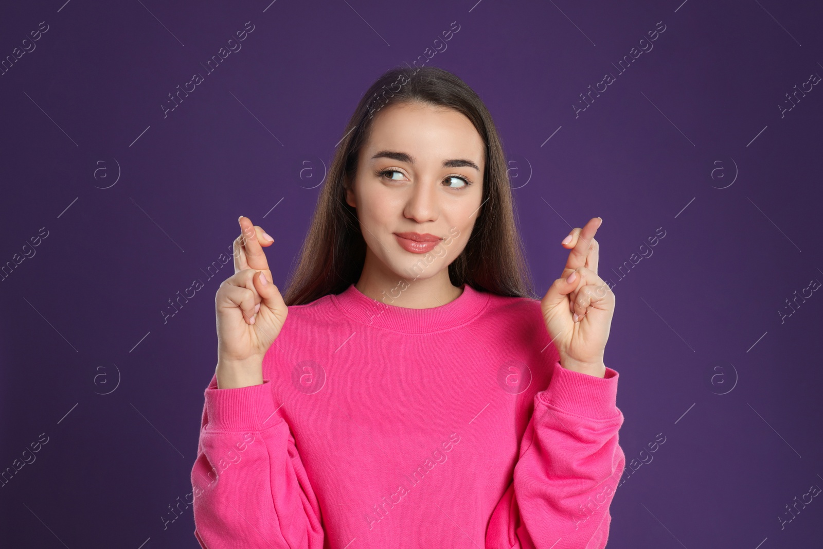 Photo of Woman with crossed fingers on purple background. Superstition concept