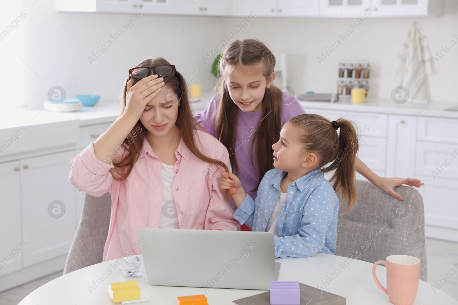 Photo of Children disturbing stressed woman in kitchen. Working from home during quarantine