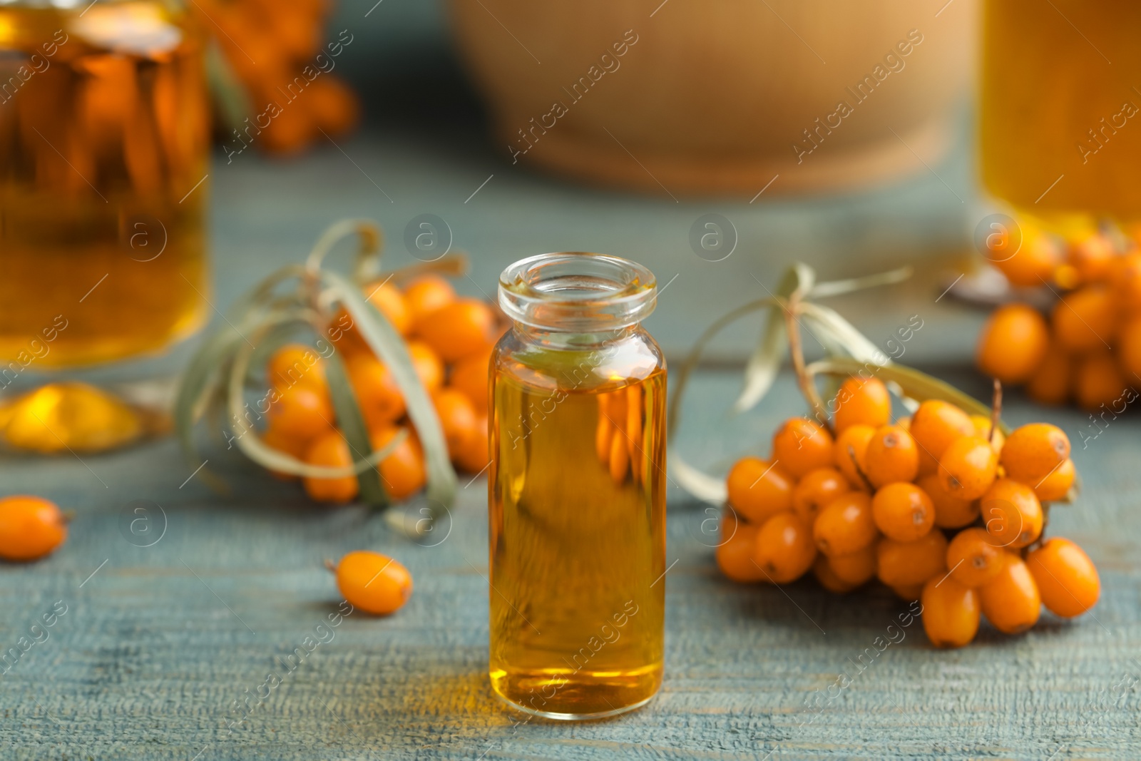 Photo of Natural sea buckthorn oil and fresh berries on blue wooden table